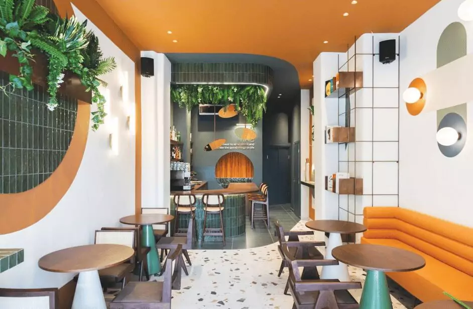 Vibrant cafe interior with green tiles, orange ceiling, and modern furniture in London by Oraanj Interior Design.
