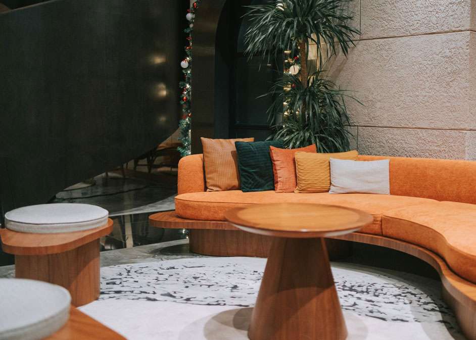 Modern lounge area in London with curved orange sofa and round wooden tables designed by Oraanj Interior Design.