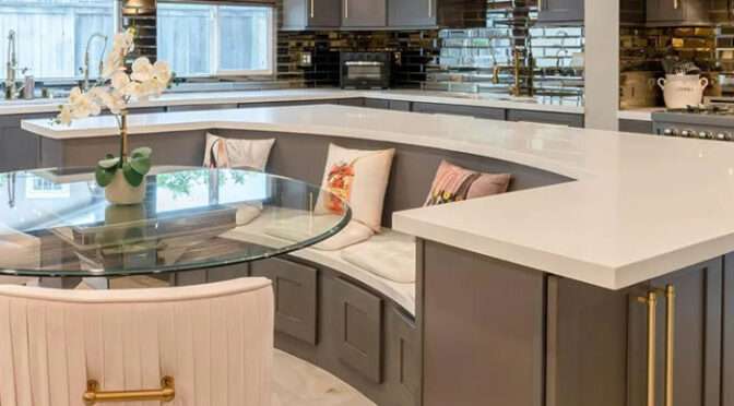 Luxury kitchen interior design in Richmond upon Thames by Oraanj Interior Design, featuring elegant chandeliers, grey cabinetry, and a built-in seating area with a glass dining table.