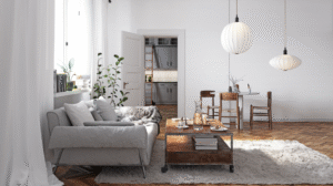Bright, minimalist living and dining space with a light grey sofa, wooden dining table, white walls, pendant lighting, indoor plants, and warm wooden flooring, filled with natural daylight.