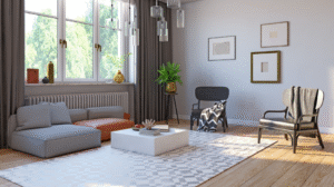Bright, modern living room with a grey sectional sofa, white geometric rug, low square coffee table, accent chairs, framed wall art, and large windows letting in natural light.