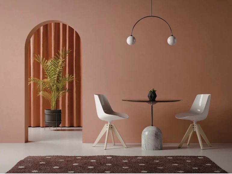 Minimalist dining nook with round table, modern chairs, arched feature wall, sculptural lighting, and warm earthy tones.