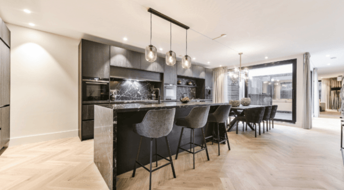 Modular kitchen design in London by Oraanj Interiors featuring dark cabinetry, a marble island, and elegant pendant lighting for a sleek and modern aesthetic.