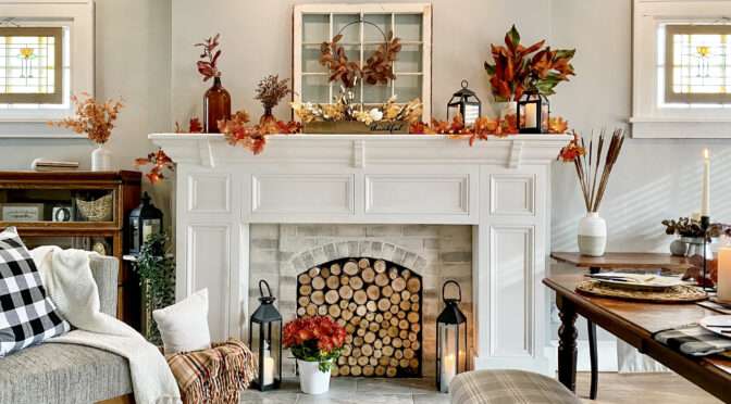 Cozy living room decorated for fall with white fireplace mantel, autumn leaves, lanterns, plaid throws, and a rustic dining table.