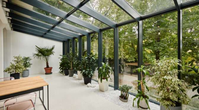 Modern garden room with glass roof, full-height windows, and indoor plants.