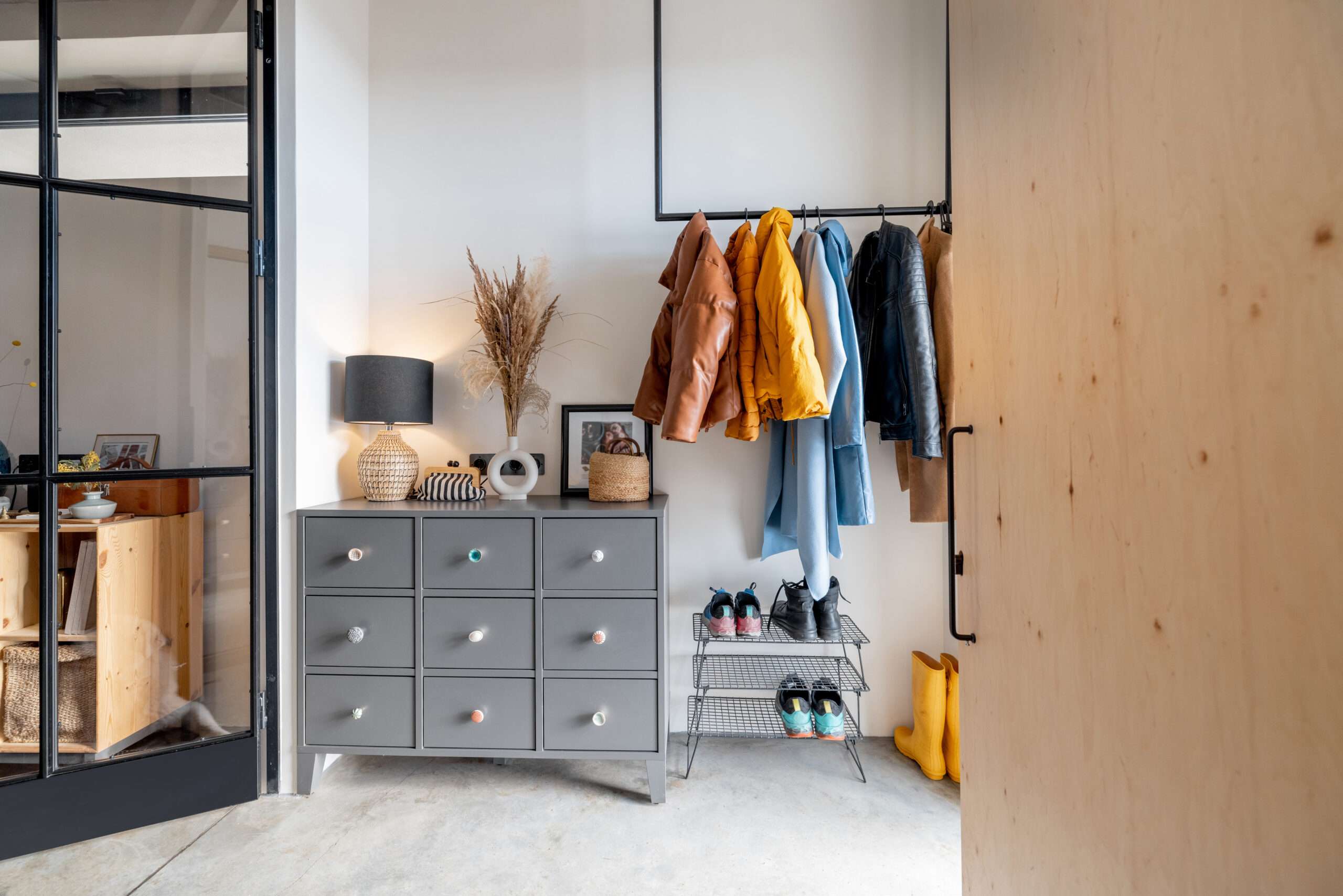 Modern hallway with gray storage cabinet, coat rack, shoes, and stylish home decor.