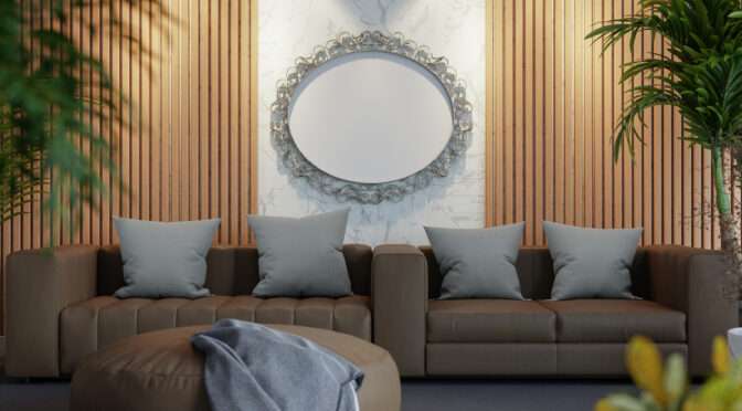 Modern living room with brown leather sofa, grey cushions, round leather ottoman, decorative oval wall mirror, and wooden slat wall with marble paneling.