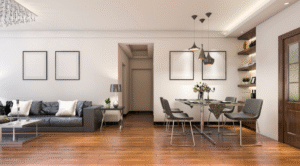 A contemporary open-plan living and dining area with a grey sofa, glass coffee table, dining table with upholstered chairs, pendant lighting, wooden flooring, and minimalist wall décor.