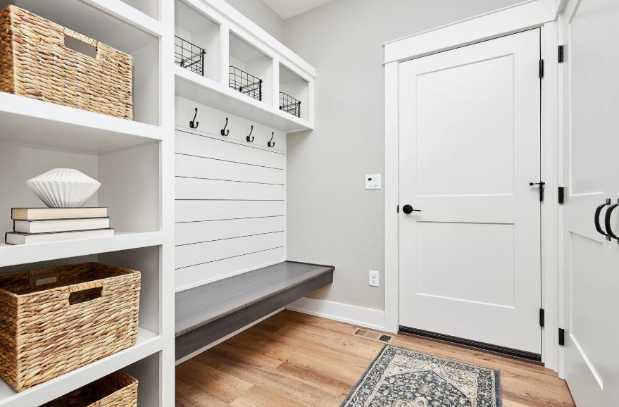 Bright mudroom interior with built-in shelving, storage baskets, wall hooks, bench seating, and wooden flooring.
