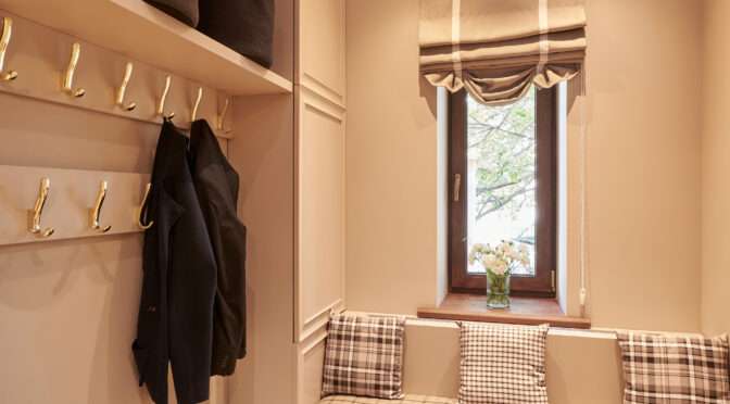 Mudroom with built-in bench seating, plaid cushions, overhead storage baskets, coat hooks, and natural wood flooring under warm lighting.