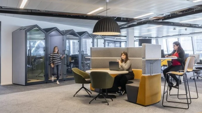 Contemporary office workspace with collaborative seating, acoustic booths, modern lighting, and employees working in an open-plan environment.