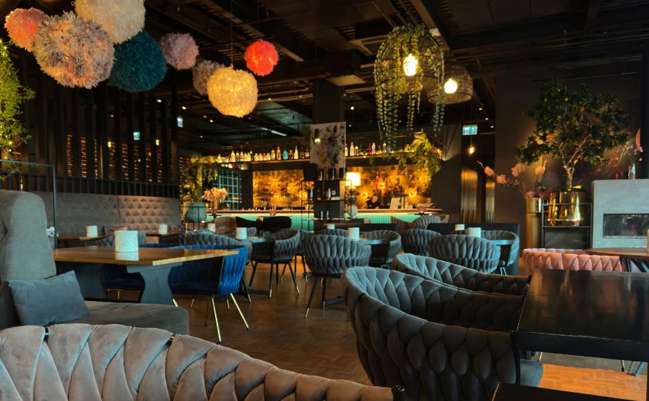 Stylish restaurant interior with plush velvet seating, warm ambient lighting, hanging decorative lights, and a lively yet intimate atmosphere.