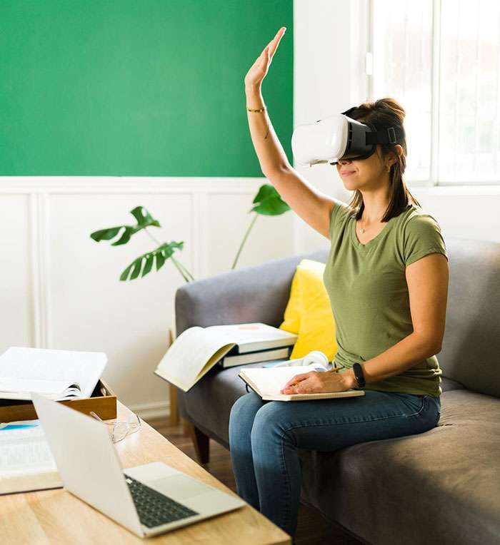 Woman using VR headset sitting on sofa in living room Woman using VR headset sitting on sofa in living room