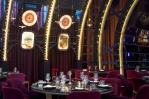 Contemporary restaurant interior with curved architectural frames, plush burgundy seating, ambient lighting, and an elegant, theatrical dining atmosphere.