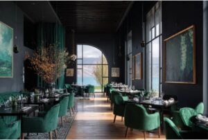 “Luxury restaurant interior with deep green upholstered chairs, dark walls, elegant table settings, framed artwork, and an arched window creating a dramatic ambience.”