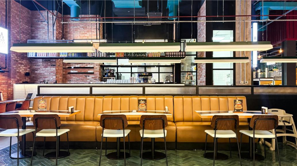 “Modern industrial bar interior with tan leather banquette seating, high bar stools, exposed brick walls, metal detailing, and statement linear pendant lighting.”