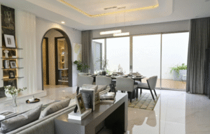 A contemporary open-plan living and dining area with a dining table and chairs, soft neutral furnishings, arched doorway, built-in shelving, large sliding glass doors, and layered ceiling lighting.