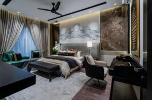 A luxurious modern bedroom with a large upholstered bed, marble accent wall, soft layered lighting, a lounge chair, a desk area, floor-to-ceiling curtains, and a ceiling fan.