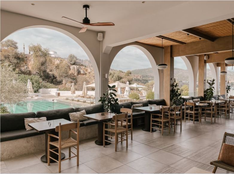 “Open-air restaurant dining area with arched openings, wooden tables and chairs, ceiling fans, neutral finishes, and scenic outdoor views.”
