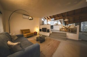 “Modern split-level living room with a sectional sofa, floor lamp, neutral rug, minimal décor, and a raised dining area with wooden furniture.”