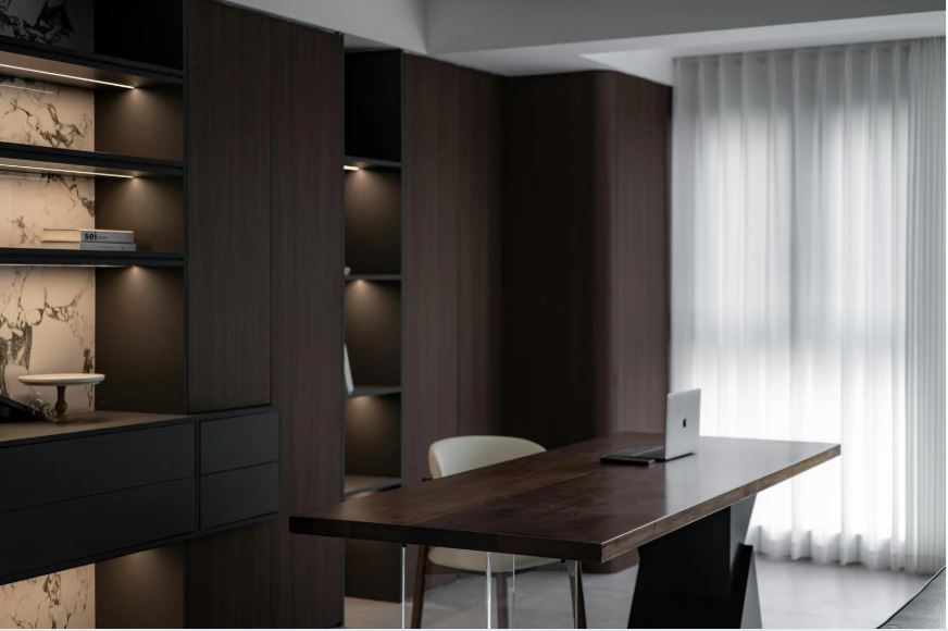 “Modern home office with a dark wood desk, built-in shelving, ambient lighting, minimalist seating, and sheer curtains allowing soft natural light.”