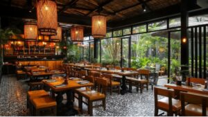 Restaurant interior with wooden tables and chairs, patterned black‑and‑white floor tiles, large woven pendant lights, and glass windows opening onto a green garden.