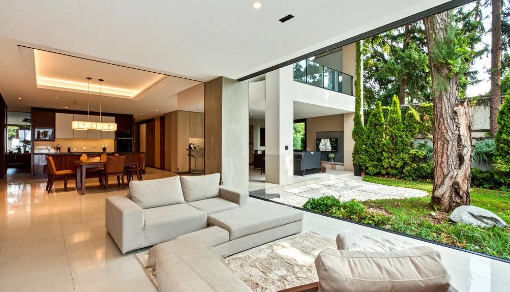 “Luxury open-plan living and dining area with neutral seating, floor-to-ceiling sliding glass doors, modern kitchen, and seamless connection to a landscaped garden.”