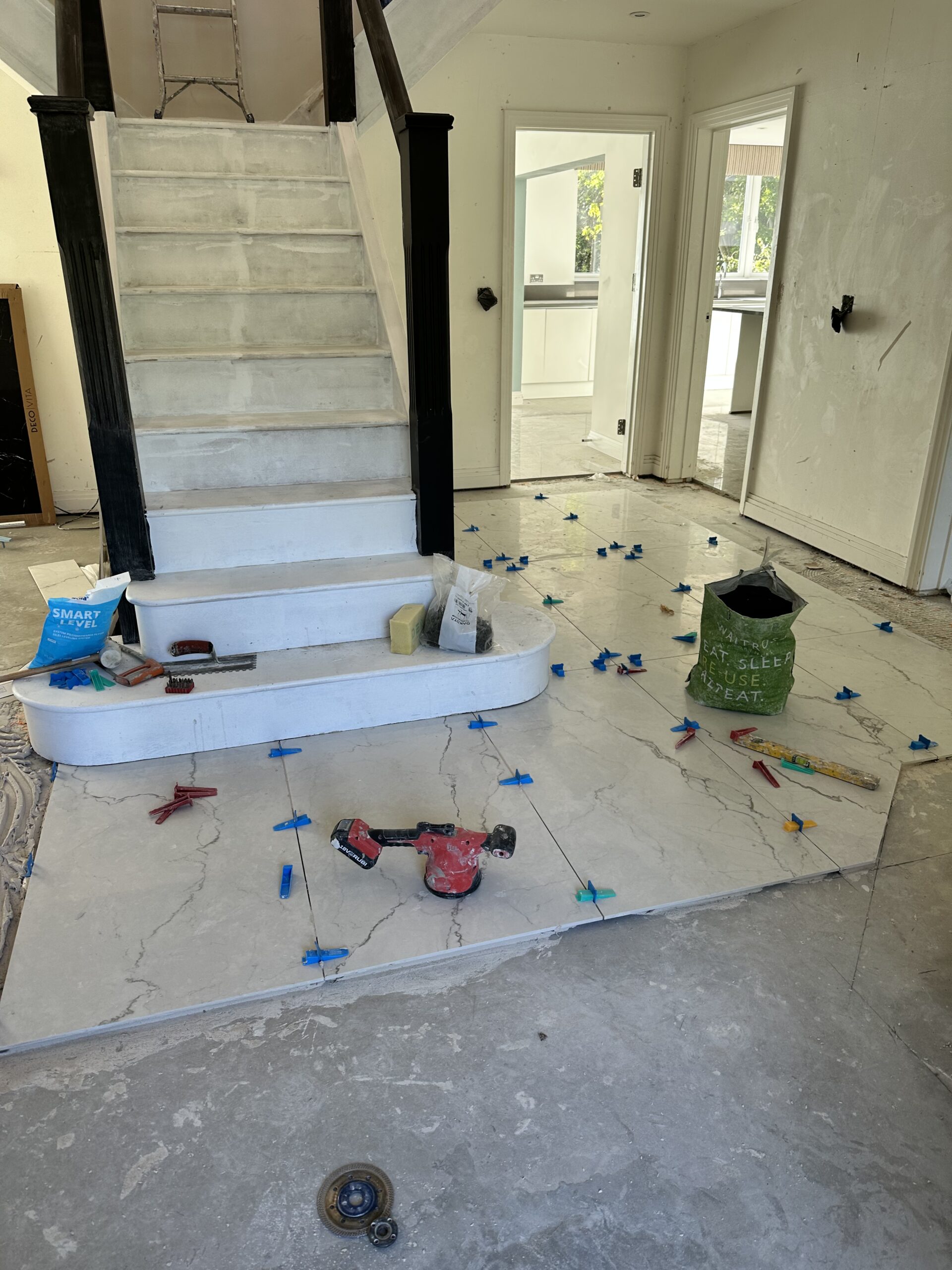 Marble Floor Tile Installation in Residential Hallway Large marble-effect porcelain floor tiles being installed in a home hallway using a professional leveling system near a white staircase.