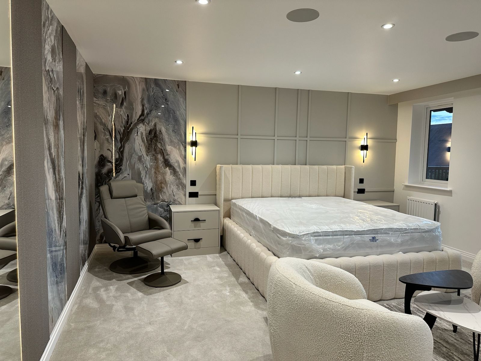 Contemporary Master Bedroom with Feature Wall in London A contemporary master bedroom featuring upholstered bed, marble-effect feature wall, ambient lighting, and bespoke bedside units, designed by Oraanj Interiors for a luxury London residence.
