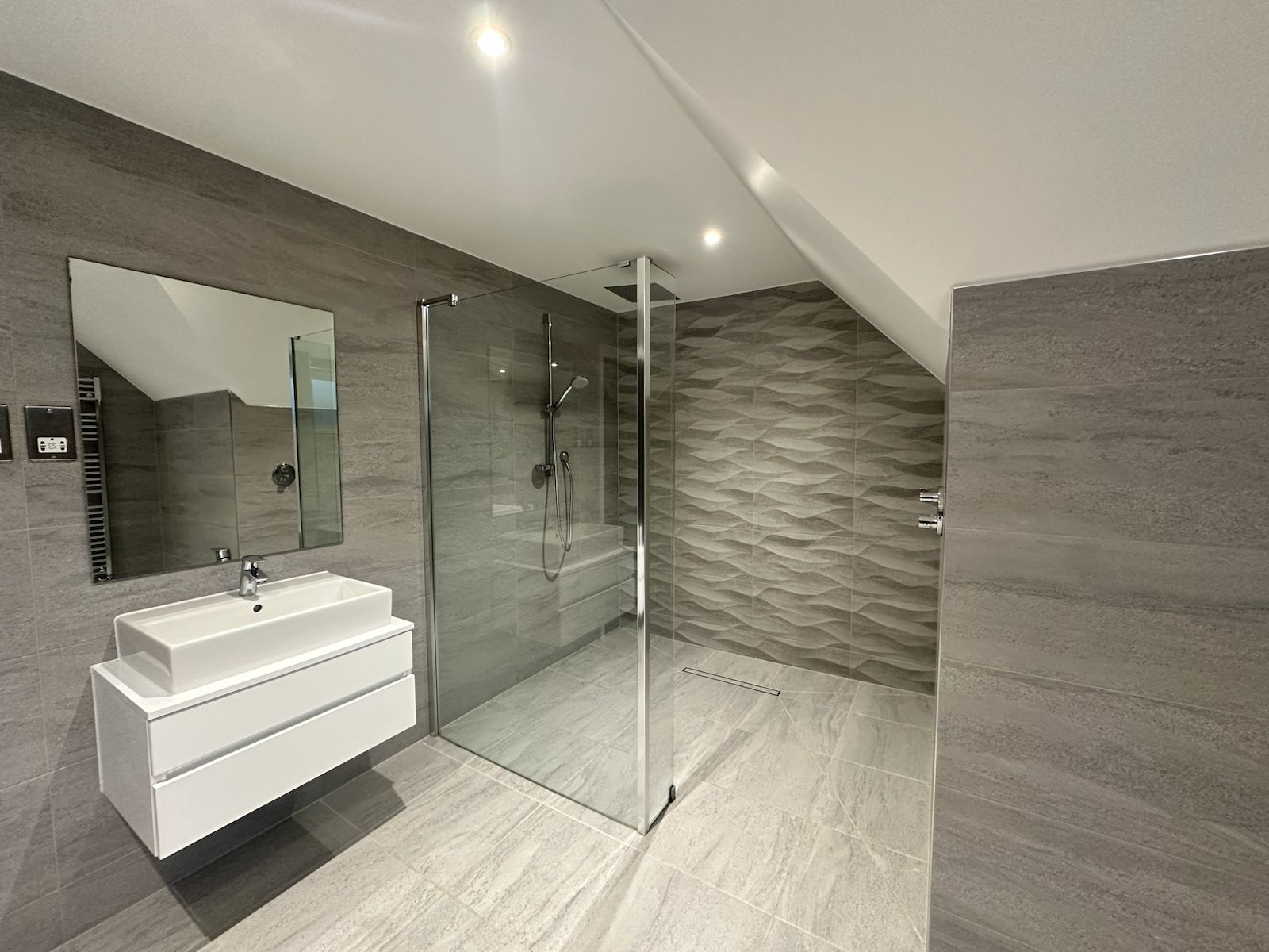 Contemporary Bathroom Design in London Residence A sleek contemporary bathroom featuring walk-in glass shower, textured wall tiles, floating vanity, and modern fixtures, created by Oraanj Interiors in London.