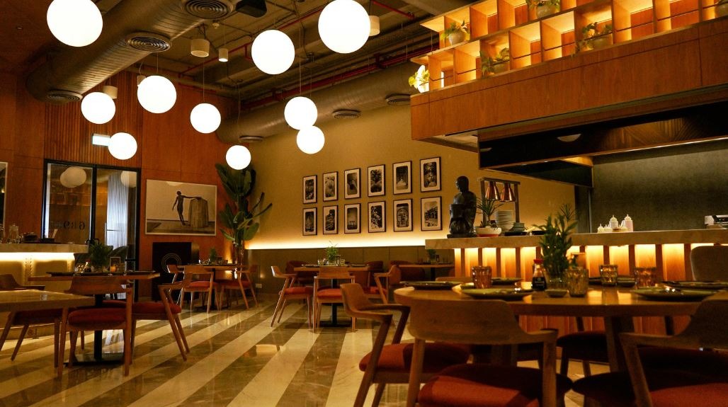 Modern restaurant interior with striped marble floor, wooden tables and red‑cushioned chairs, large white spherical pendant lights, exposed ducts, and framed artwork on warm beige walls.